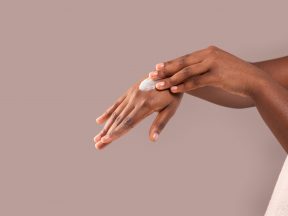 Eine Person trägt einen Klecks Lotion auf ihren Handrücken auf und zeigt „Händepflege Haut“ vor einem schlichten beigen Hintergrund.