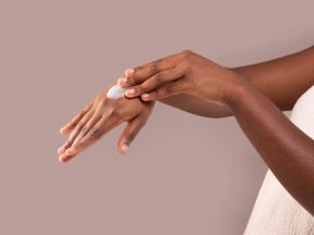 Dry Skin Treatment. Unrecognizable African American Woman Applying Moisturizing Cream On Hands Eine Person trägt einen Klecks Lotion auf ihren Handrücken auf und zeigt „Händepflege Haut“ vor einem schlichten beigen Hintergrund.